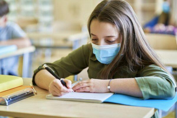 Close up of schoolgirl in protective mask writing in notebook